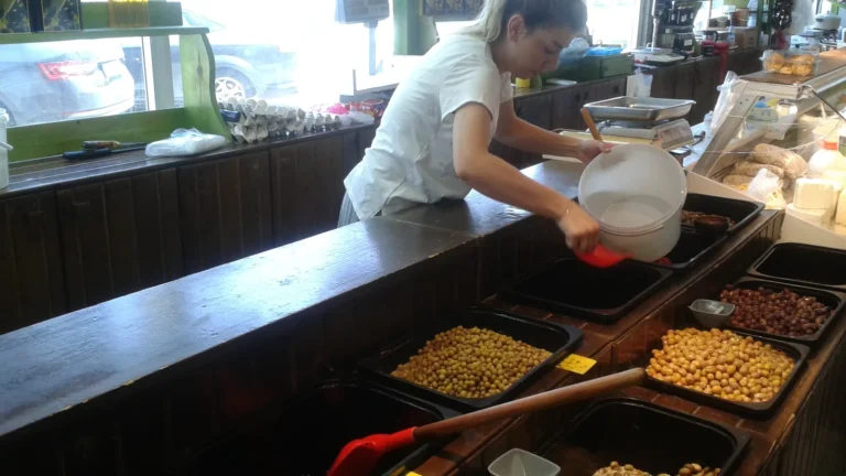 A market vendor pouring brine over trays of olives for sale