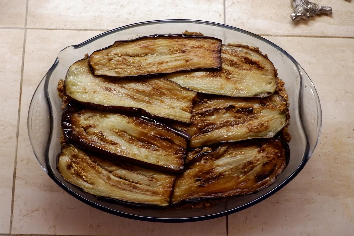 Golden aubergine slices layered in a glass baking dish while preparing moussaka