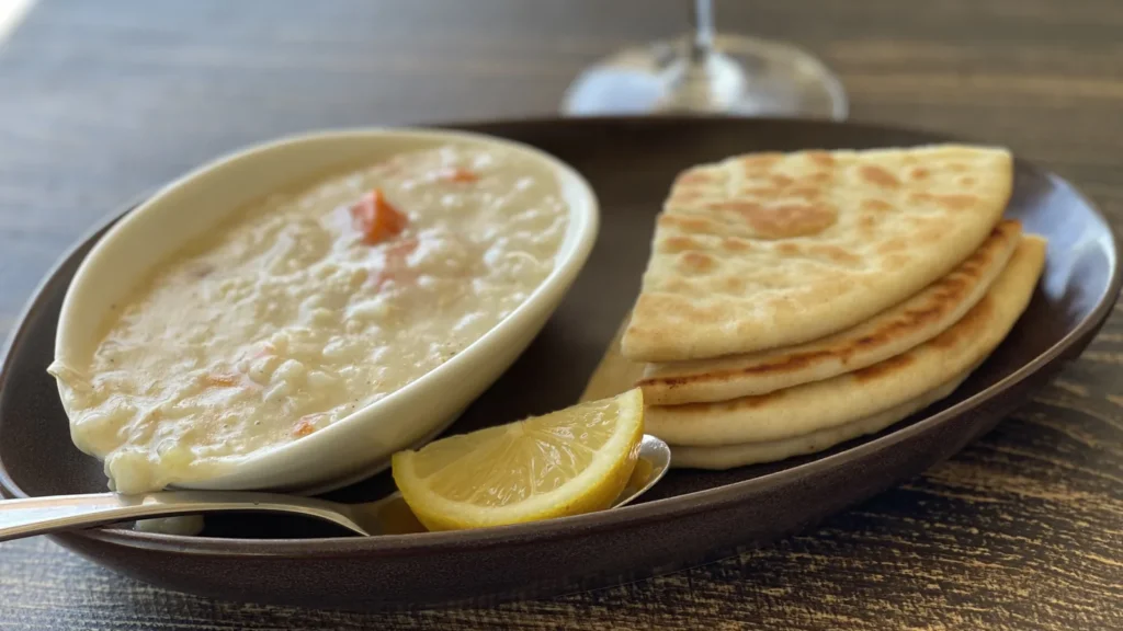 A bowl of creamy Greek avgolemono soup with lemon wedges and warm pita bread