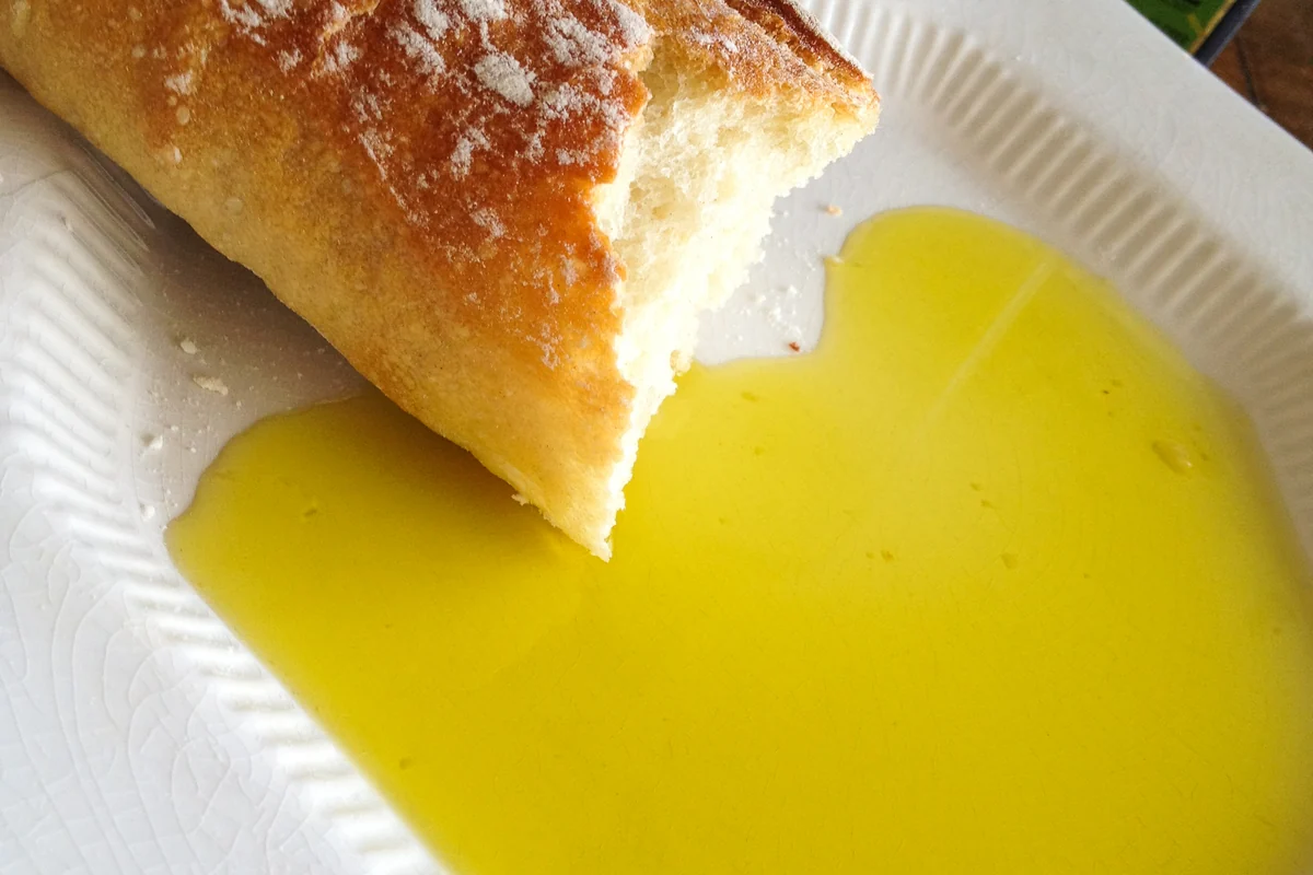 Crusty baguette beside a pool of extra virgin olive oil for dipping