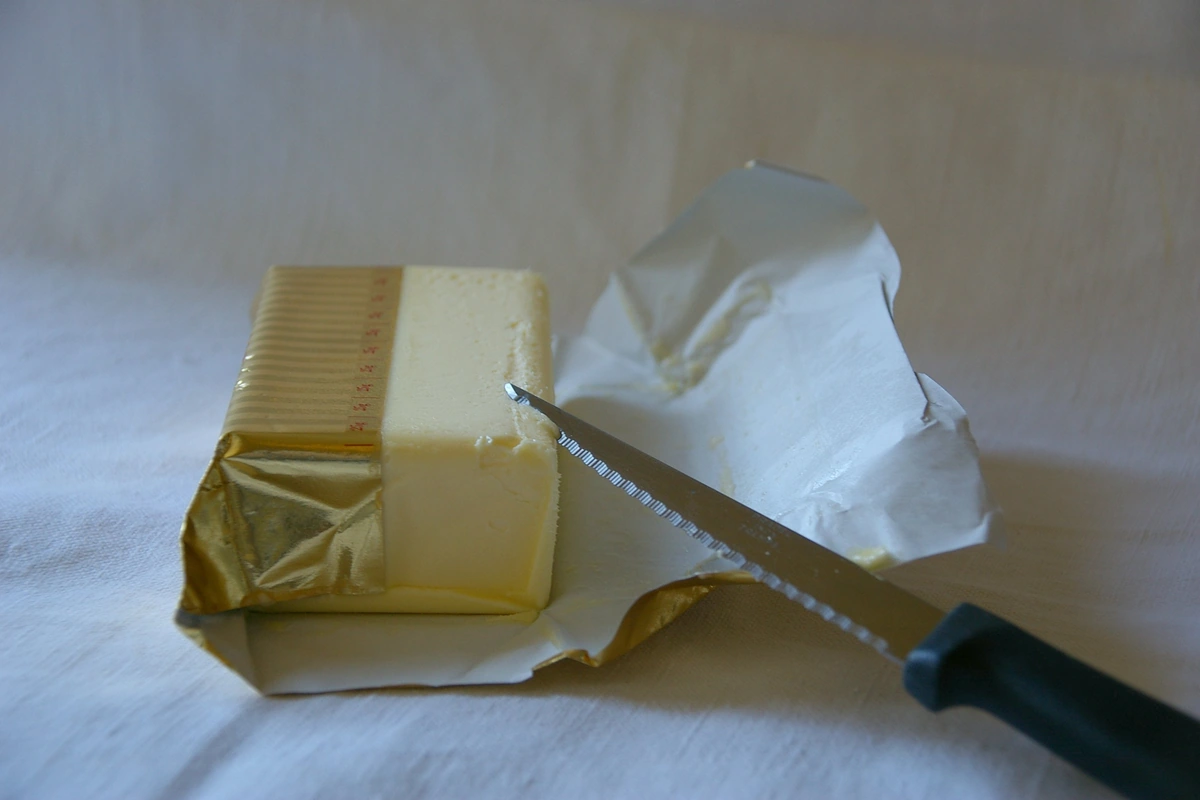 A block of butter partly unwrapped, with a knife beside it