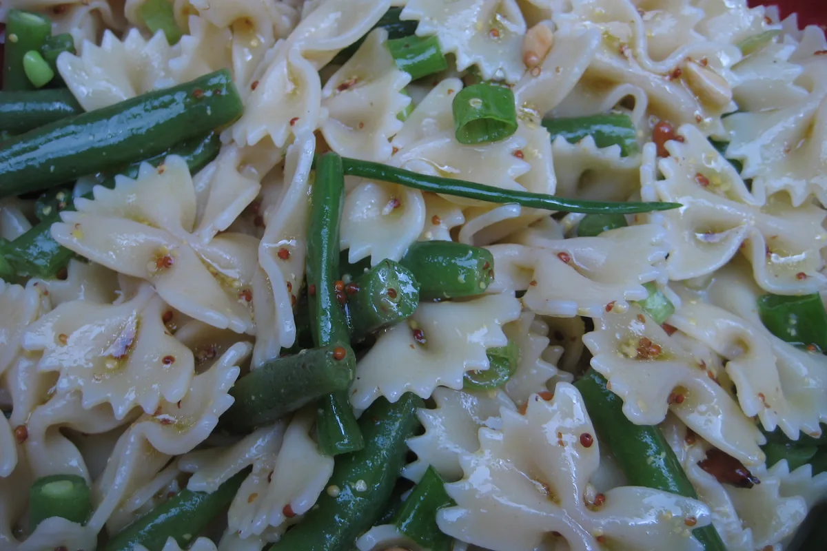 Close-up of a bowl of farfalle pasta salad with green vegetables and spring onions