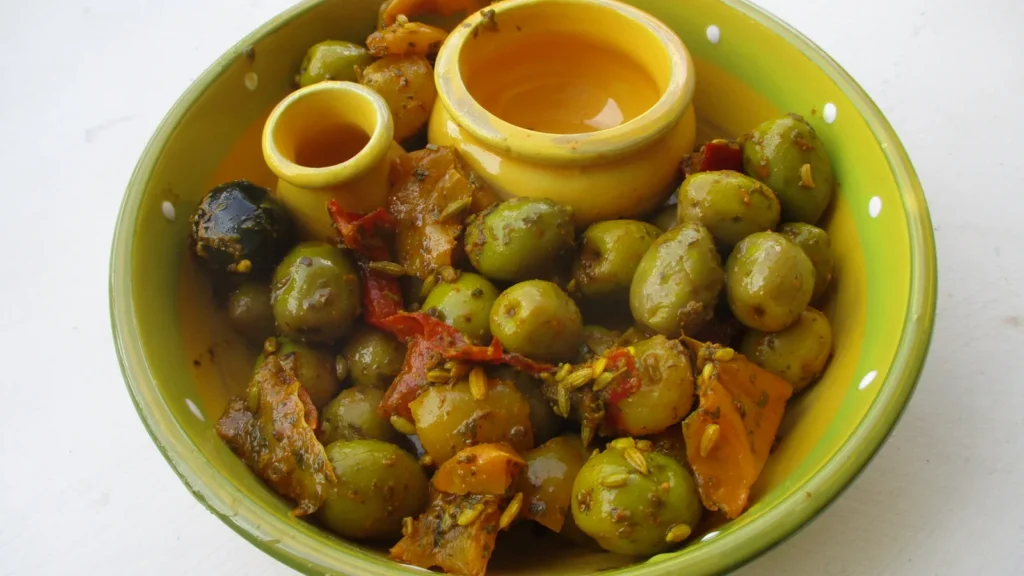 A yellow bowl of green olives marinated with herbs and vegetables, Provence style