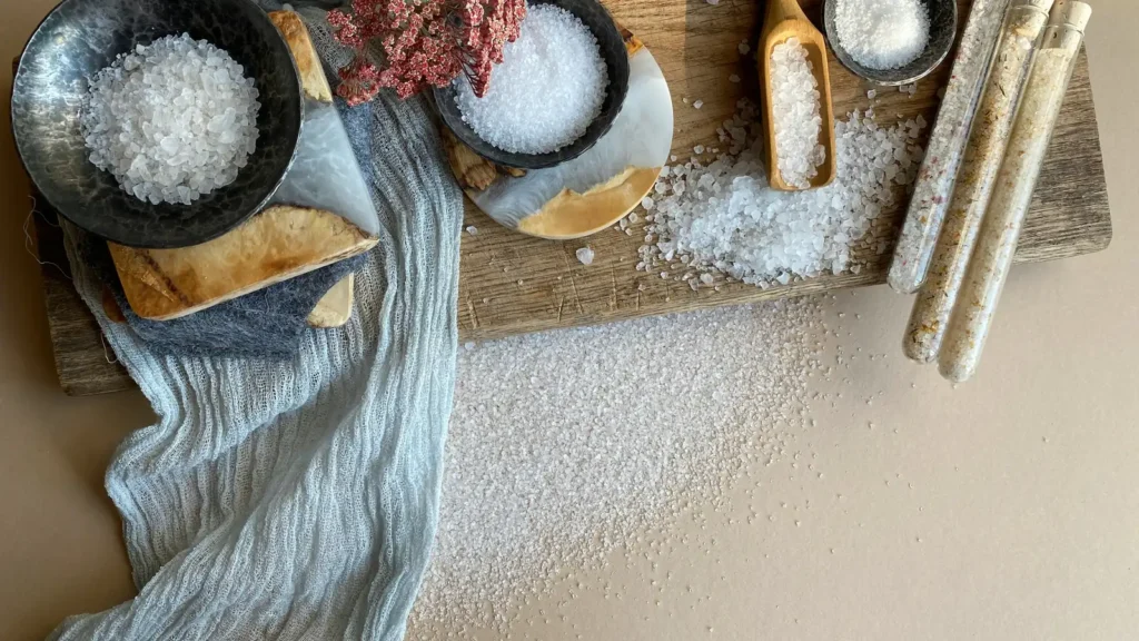 Bowls and spoons of coarse and fine salt on a wooden board, comparing sea salt vs table salt