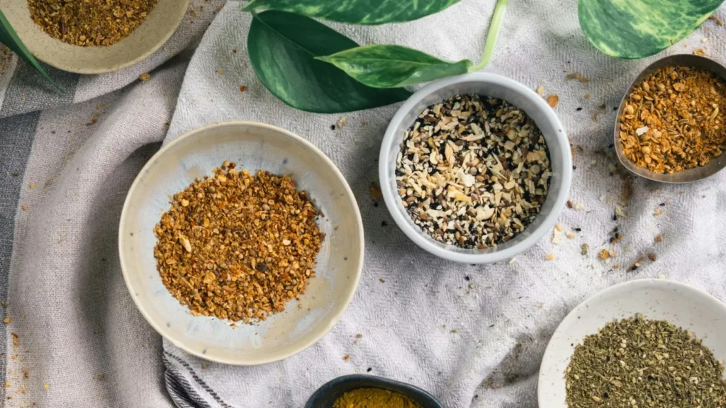 Small bowls of dried herbs and spice blends laid out for a homemade Greek seasoning recipe