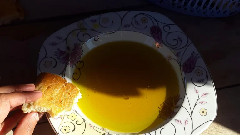 A piece of bread being dipped into a shallow bowl of golden olive oil