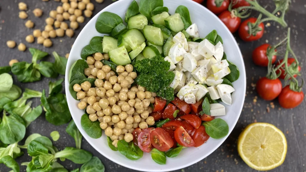A bowl of chickpea salad with cucumber, cherry tomatoes, white cheese and herbs