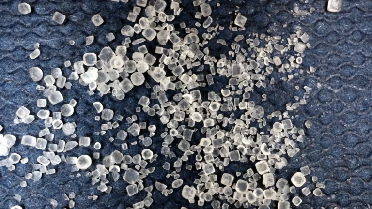 Close-up of coarse, sparkling sea salt crystals on a dark surface