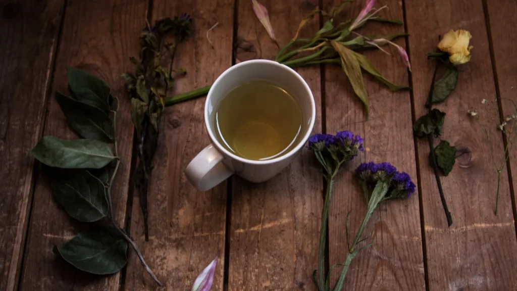 Cup of herbal tea on a wooden table with dried herbs and flowers, as when you make oregano tea