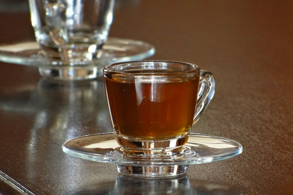 A glass cup of amber tea sweetened with honey on a saucer