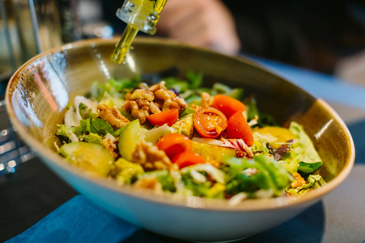 Dressing drizzled over a bowl of mixed salad with tomatoes and walnuts