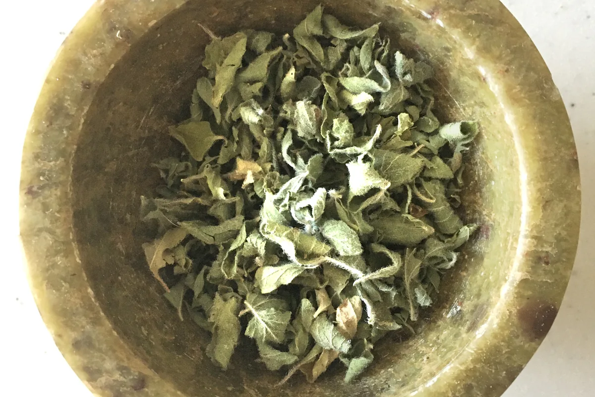 Dried oregano leaves in a small wooden bowl