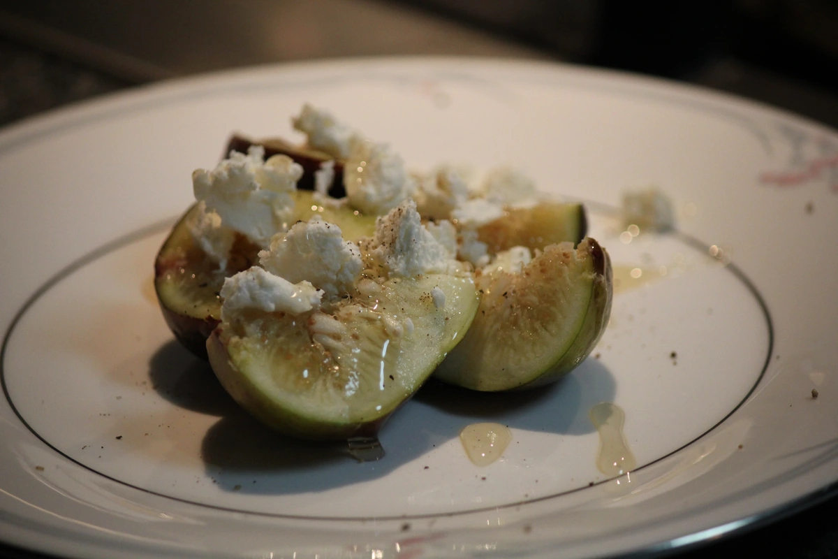 Fresh figs halved and topped with goat cheese, black pepper and honey on a white plate