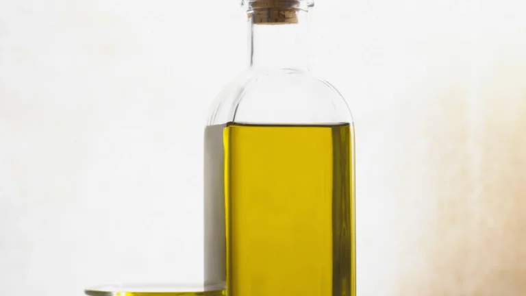 A corked glass bottle of golden olive oil against a pale background