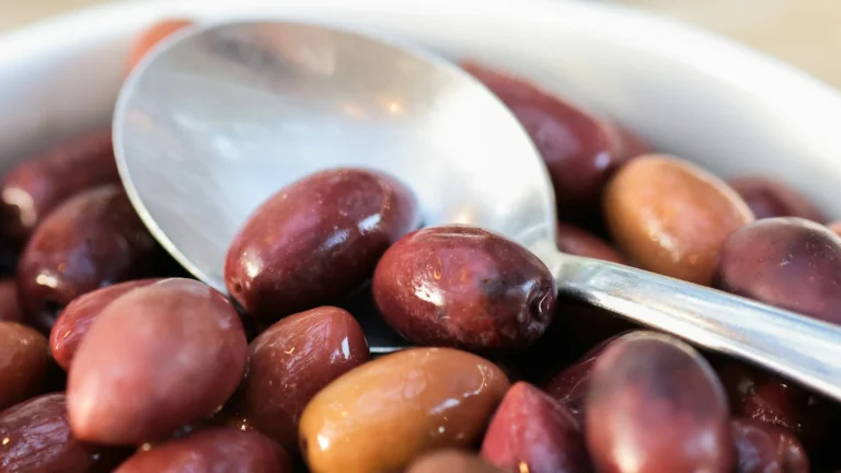 Bowl of glossy purple Greek olives with a serving spoon, for comparing Kalamata olives nutrition