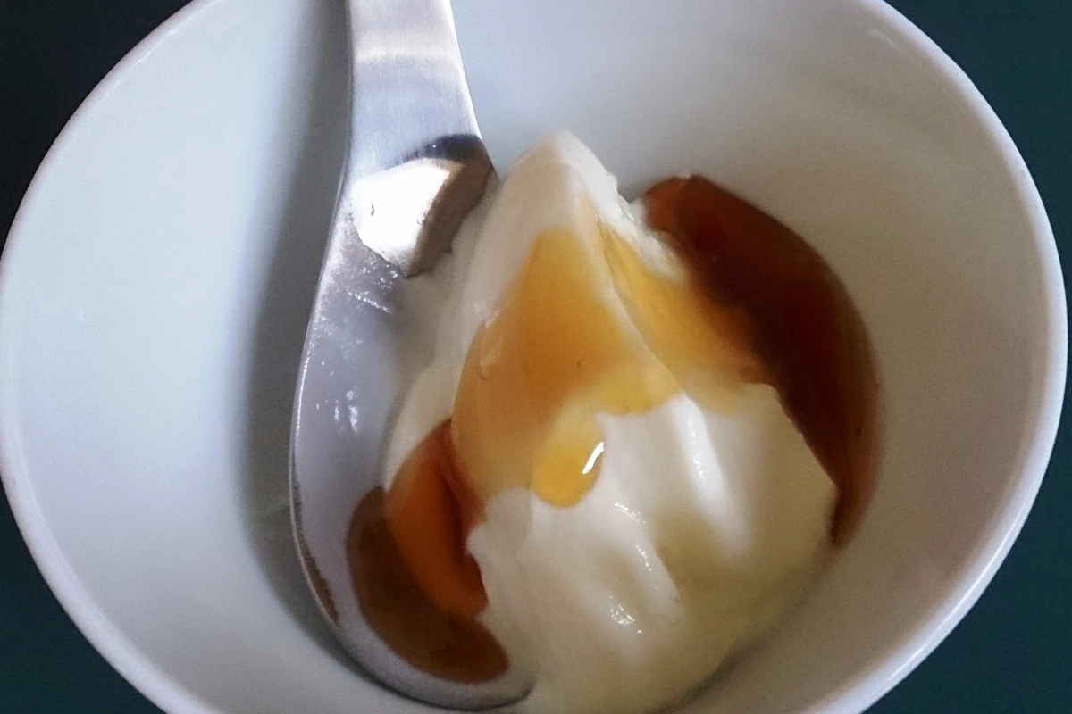 A bowl of thick Greek yogurt topped with honey, with a spoon