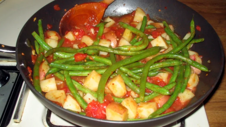 Green beans and potatoes cooking in a chunky tomato sauce in a frying pan
