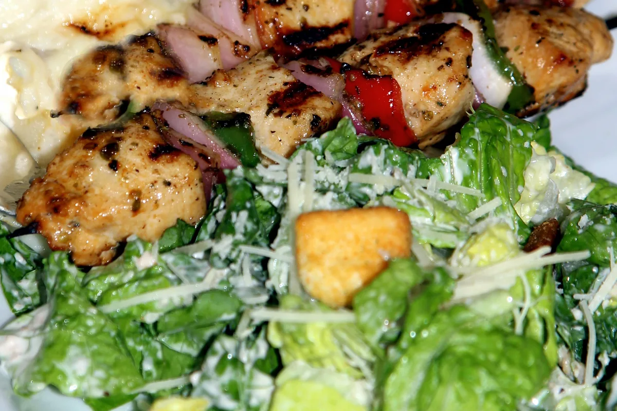 Grilled pieces of marinated chicken served over a salad