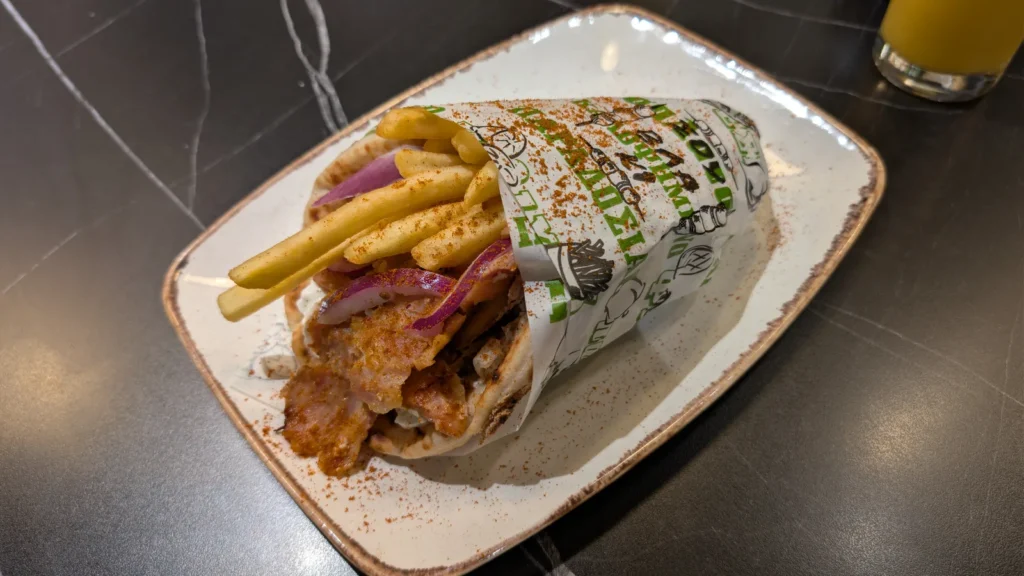 A gyros pitta wrap with sliced meat, tomato, onion, tzatziki and chips