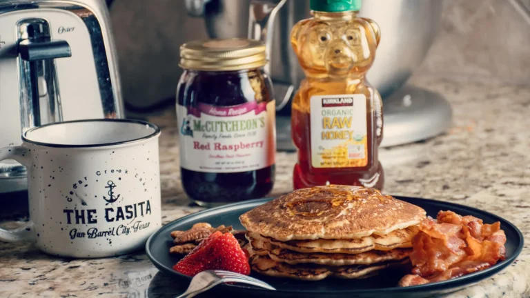 Bottles and jars of honey beside a white coffee mug on a breakfast table