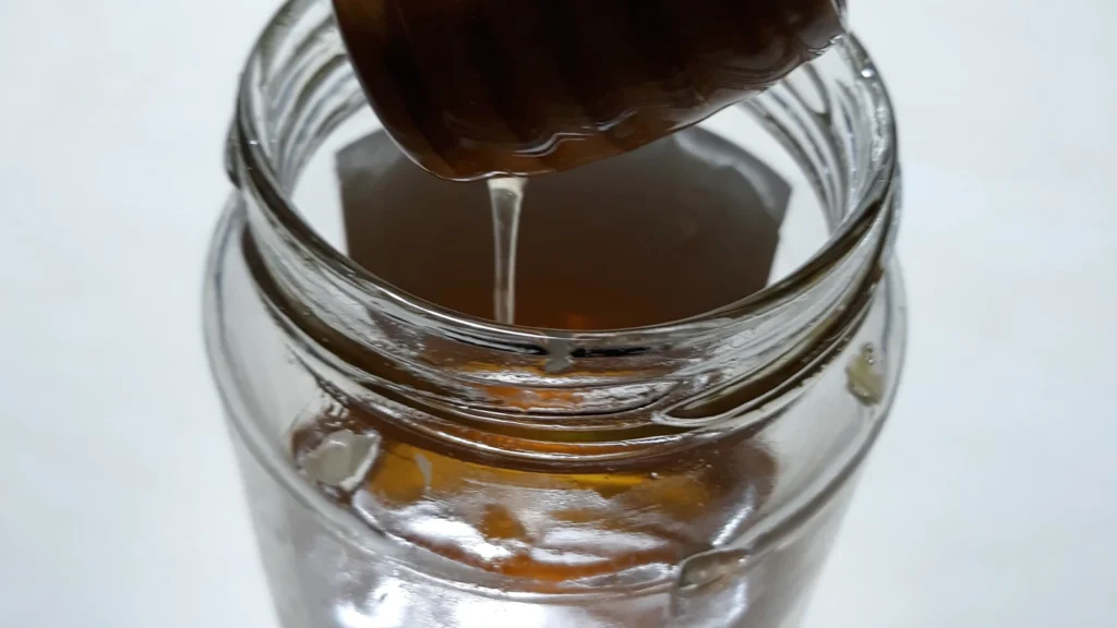 Honey dripping from a wooden honey dipper into a glass jar