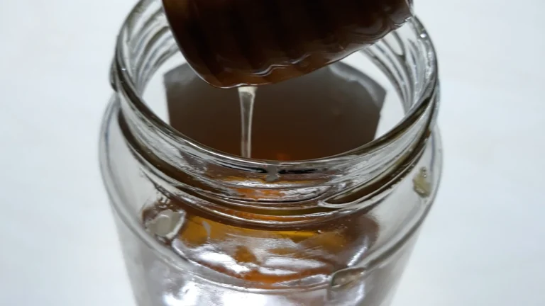 Honey dripping from a wooden honey dipper into a glass jar