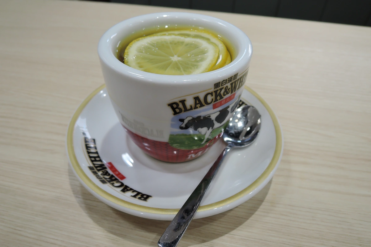 A cup of hot water with lemon slices and honey, served on a saucer with a spoon