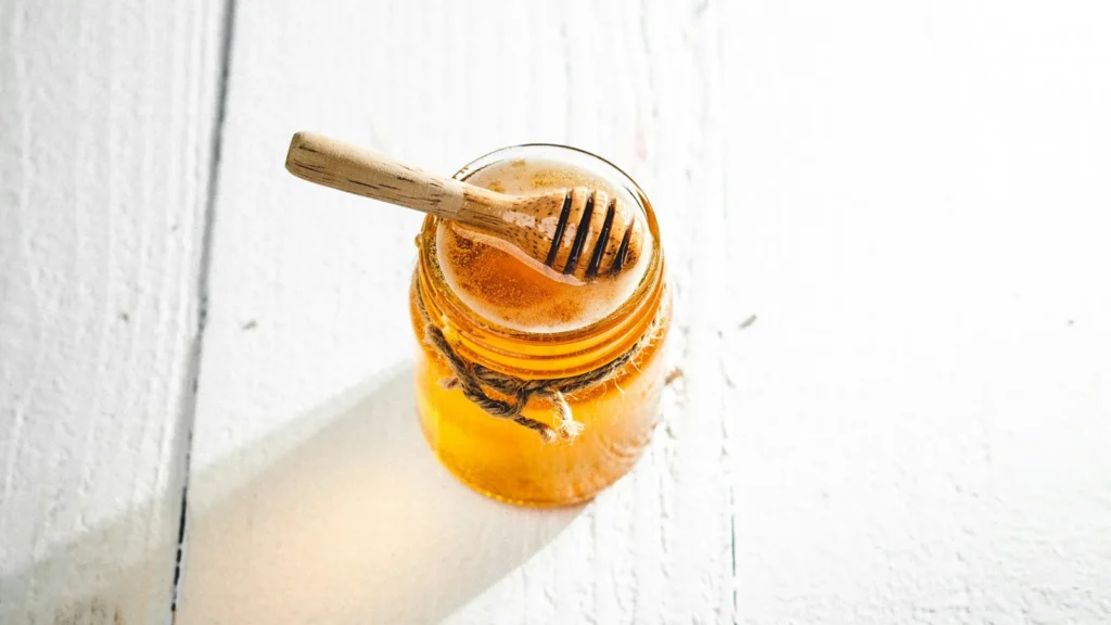 Jar of golden honey with a wooden dipper on a white wooden table, for reading honey nutrition facts