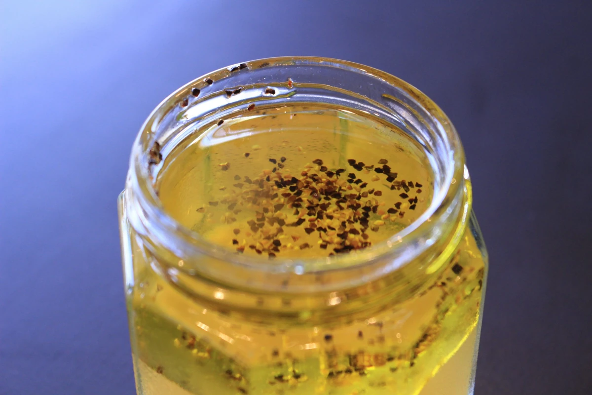 A glass jar of oil-based vinaigrette with herbs and black pepper