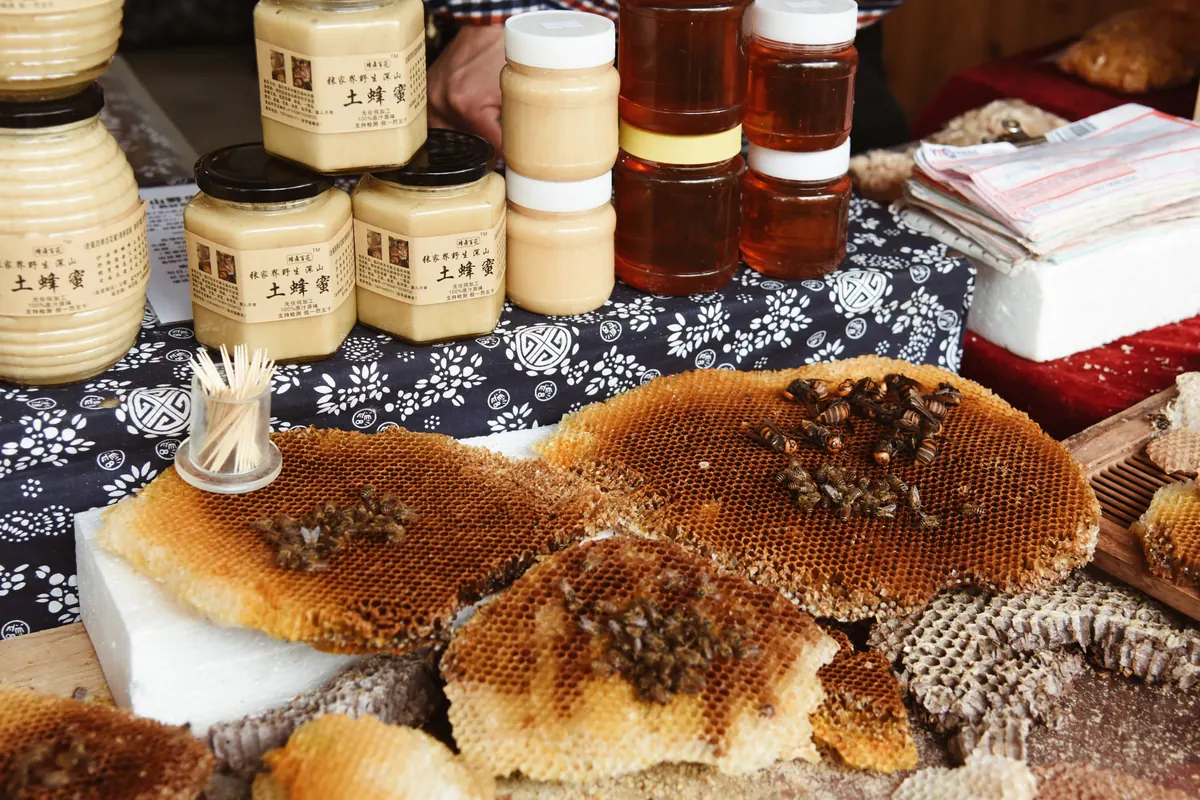 Jars of raw honey on a market stall with pieces of honeycomb
