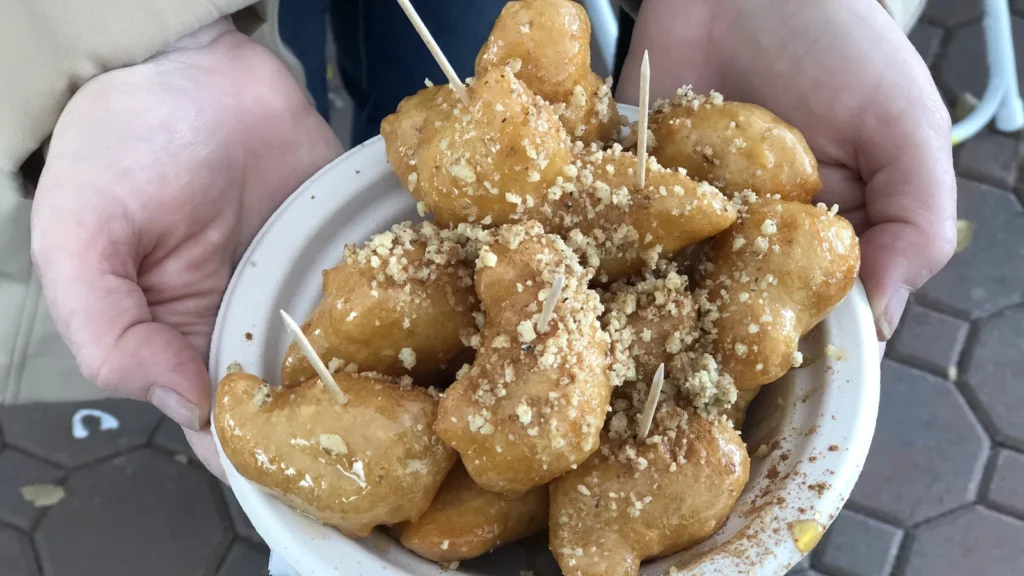A bowl of loukoumades, Greek honey doughnut puffs, drizzled with honey and sprinkled with chopped walnuts at a Greek festival
