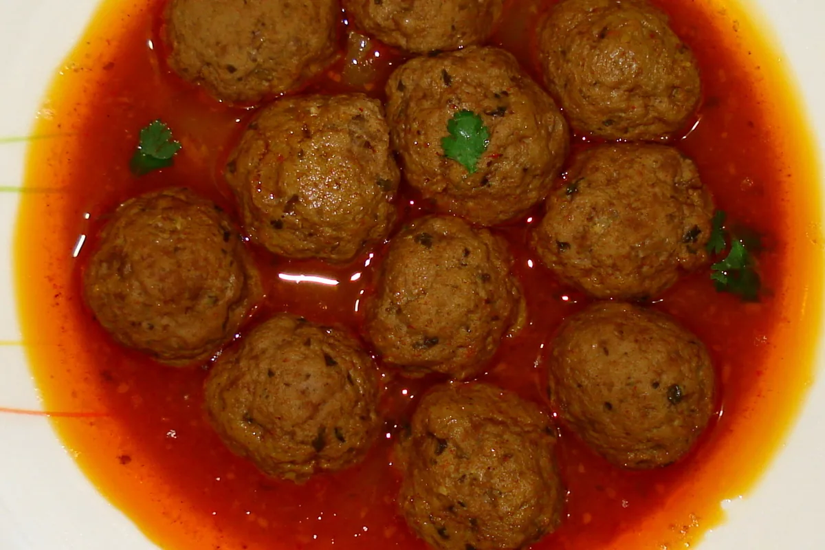 Round meatballs simmered in a red spiced sauce, garnished with herbs