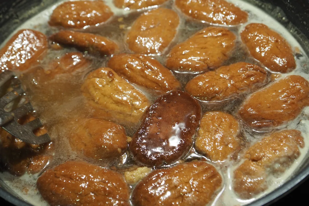 Freshly baked melomakarona soaking in honey syrup in a pan