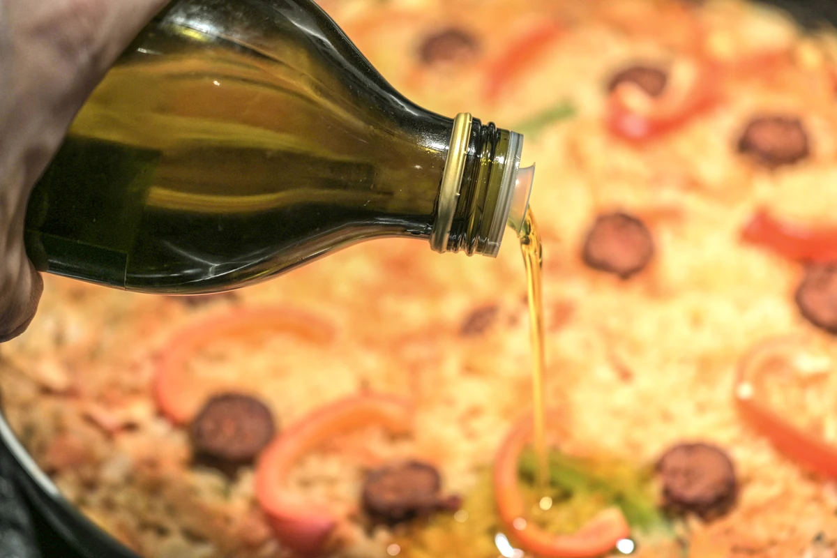 Olive oil being poured from a bottle over a pizza
