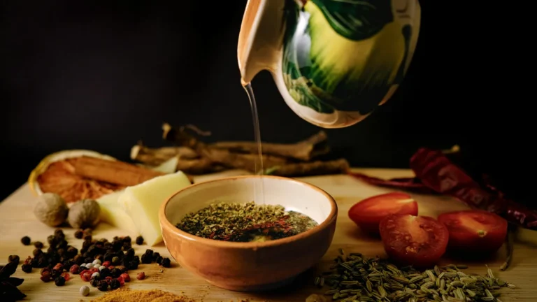 Olive oil pouring from a ceramic jug beside herbs, tomatoes and spices, illustrating olive oil nutrition facts