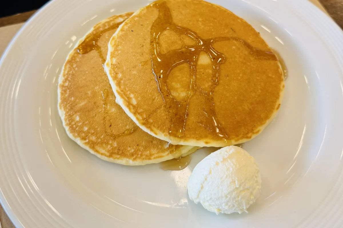 A stack of pancakes with maple syrup and a scoop of butter on a white plate