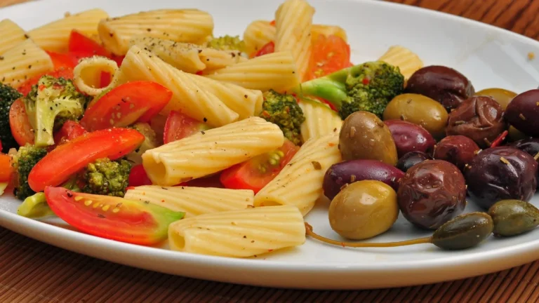A plate of pasta salad with peppers, broccoli and black and green olives