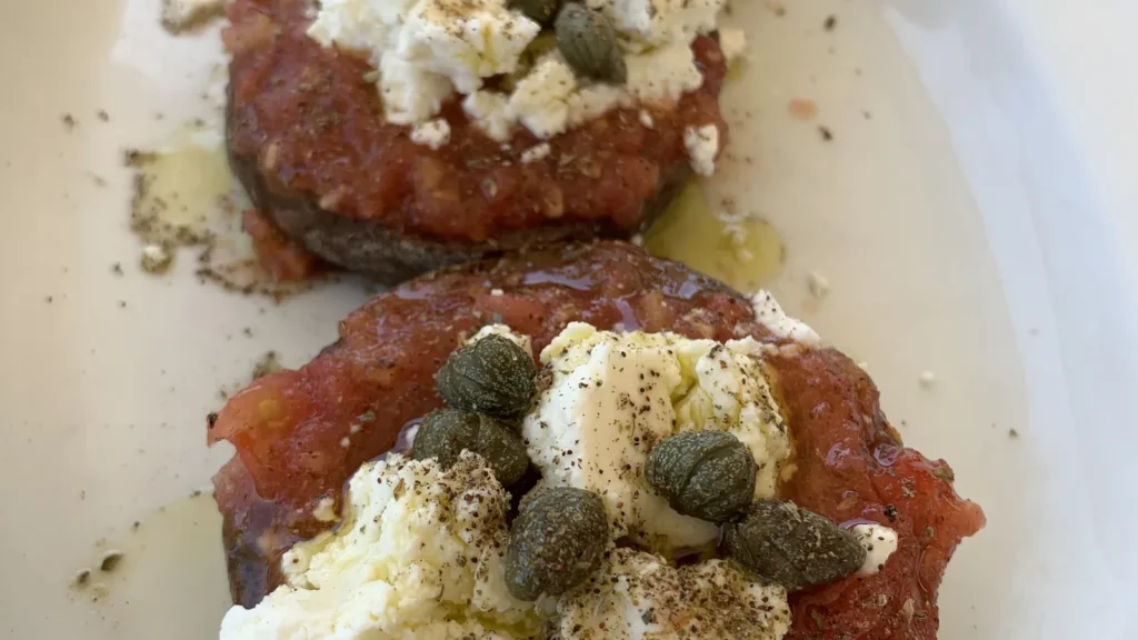 A plate of Cretan dakos: barley rusks topped with grated tomato, white cheese, capers and oregano
