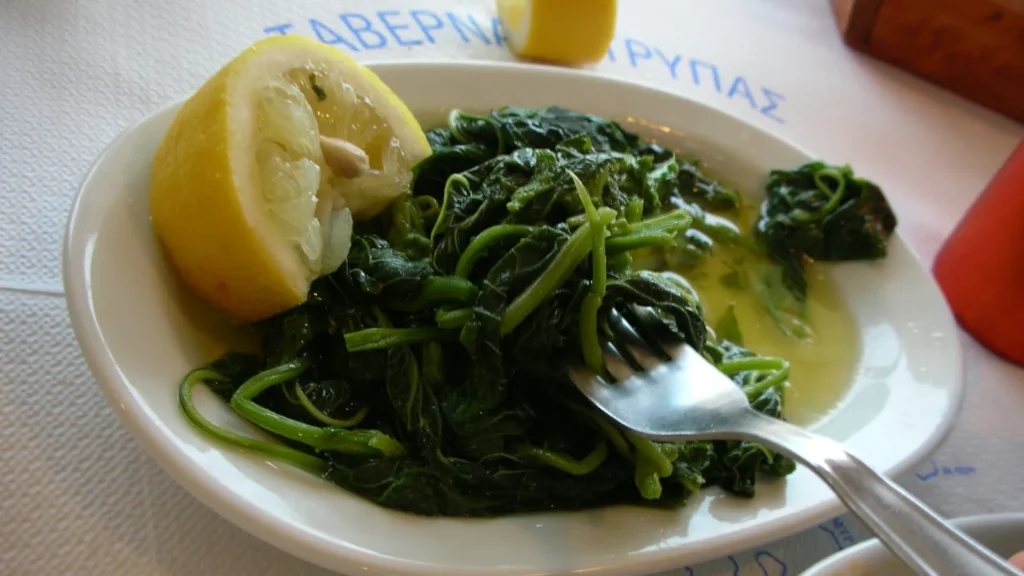 A plate of boiled amaranth greens (horta vlita) dressed with olive oil, with a lemon half on the side