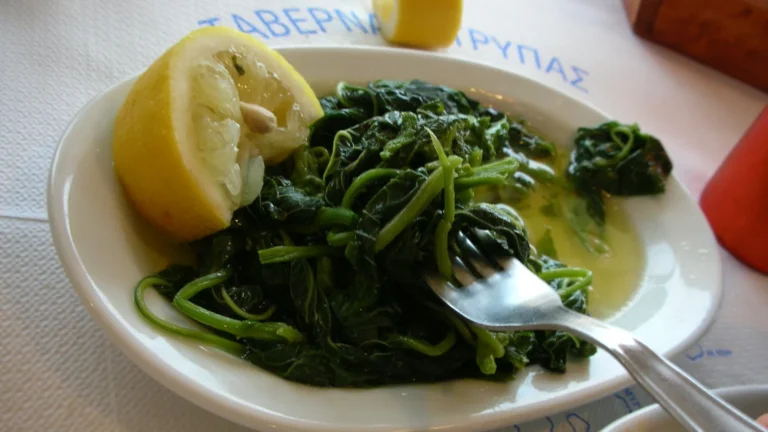 A plate of boiled amaranth greens (horta vlita) dressed with olive oil, with a lemon half on the side