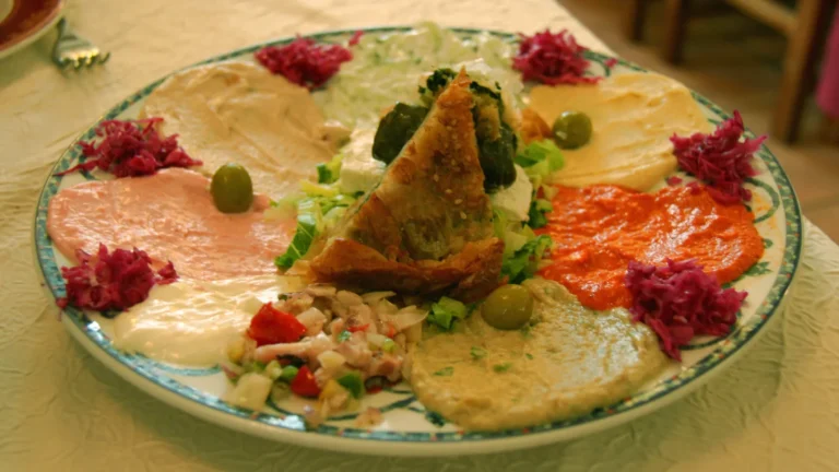 A platter of Greek dips including pink taramasalata and tzatziki, garnished with tomato and herbs