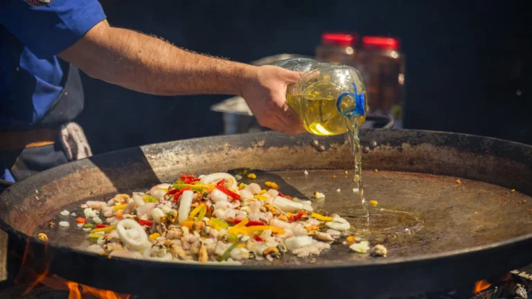 Oil being poured into a wide pan over an open fire, the moment olive oil smoke point matters