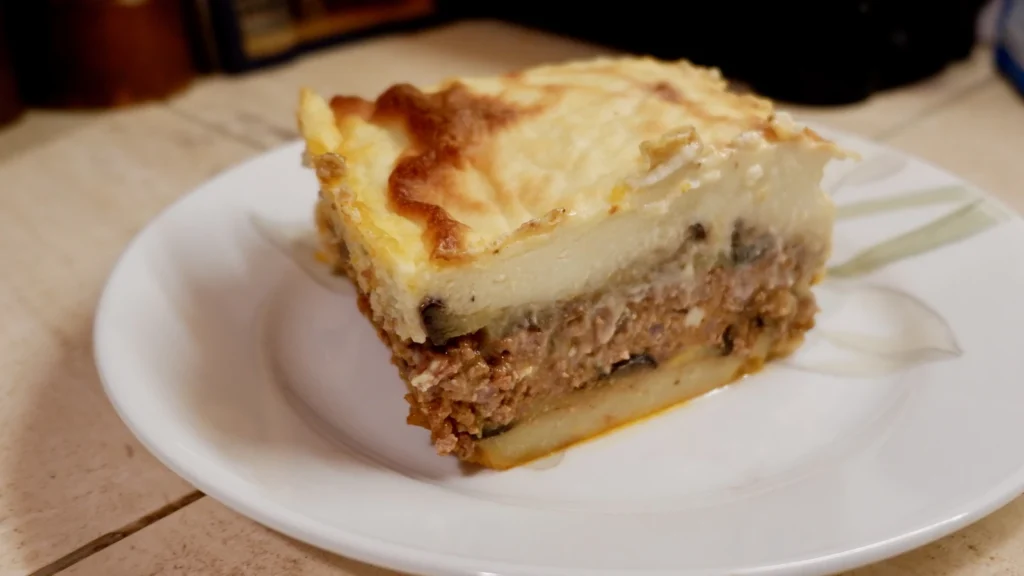 A slice of moussaka showing layers of aubergine, meat sauce and a thick golden béchamel top