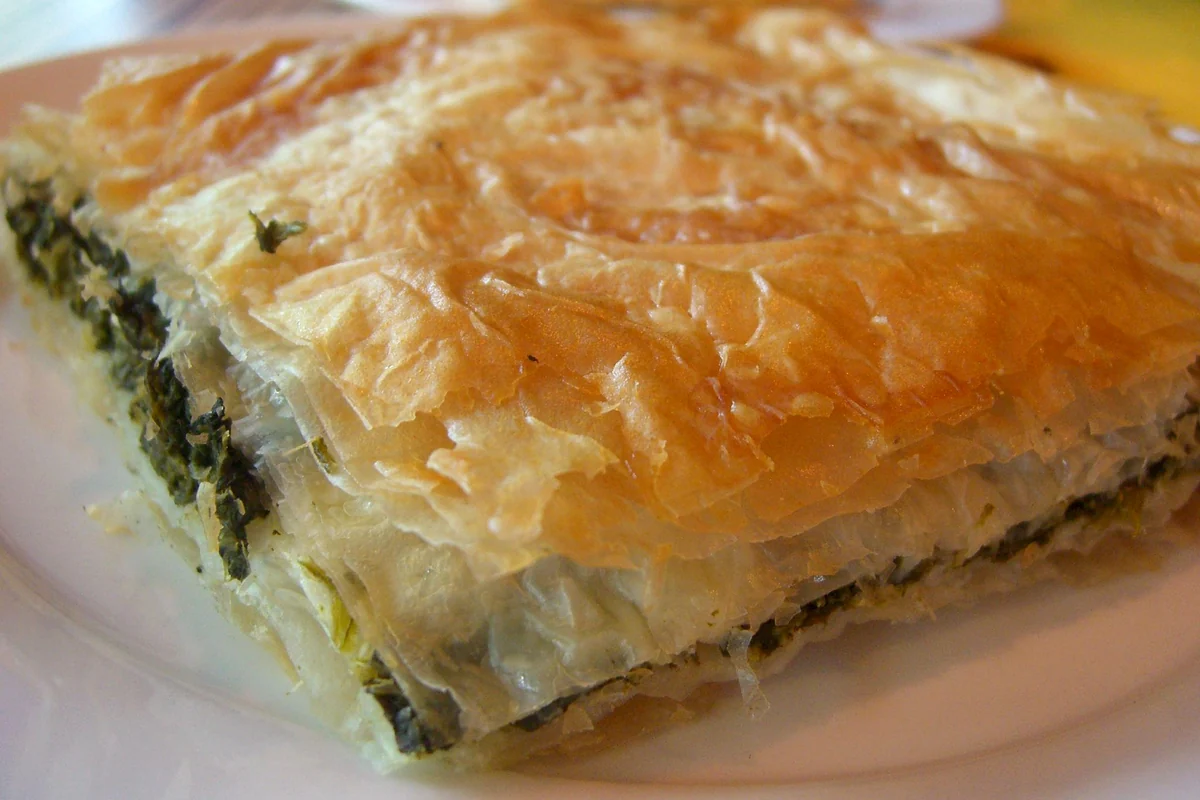 Close-up of a slice of spanakopita showing the green spinach filling between layers of phyllo