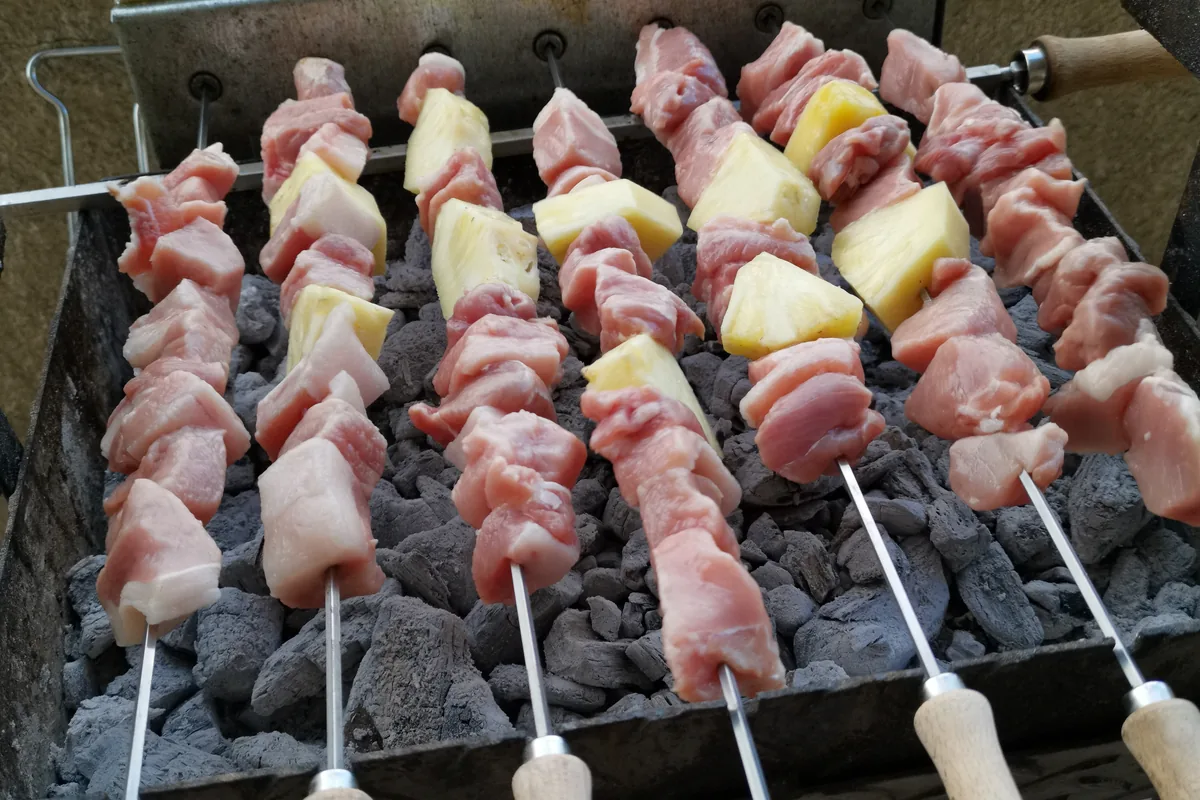 Raw souvlaki skewers of meat and onion cooking on a charcoal grill