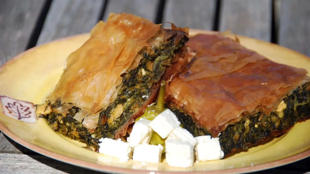 Two pieces of Greek spanakopita spinach pie with flaky phyllo and cubes of feta on a yellow plate