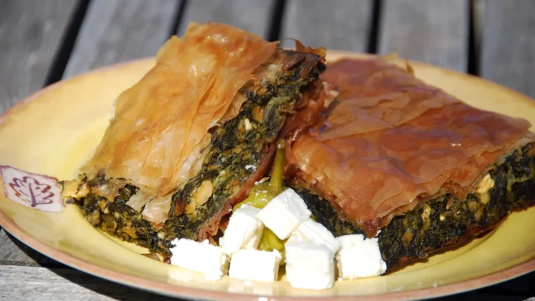 Two pieces of Greek spanakopita spinach pie with flaky phyllo and cubes of feta on a yellow plate