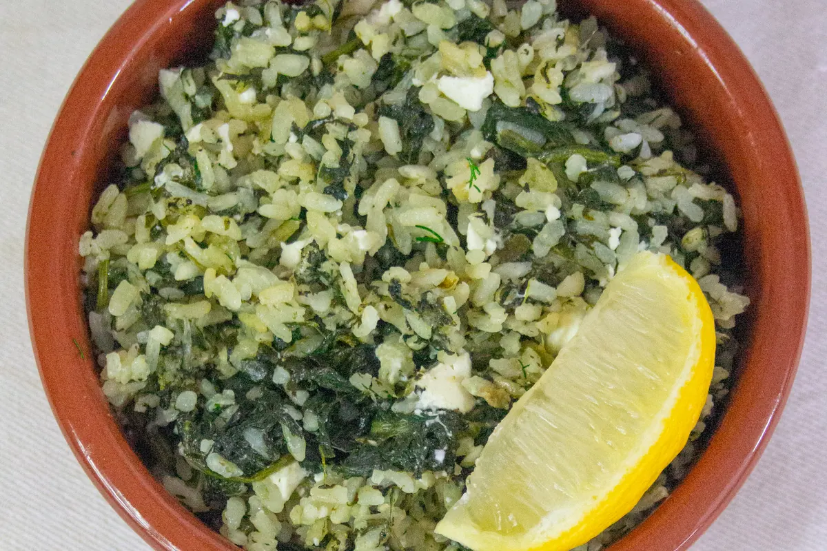 A clay bowl of spanakorizo, spinach and rice, served with a lemon wedge