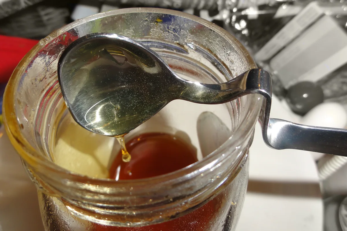 A spoon lifting golden honey from a glass jar of Greek honey