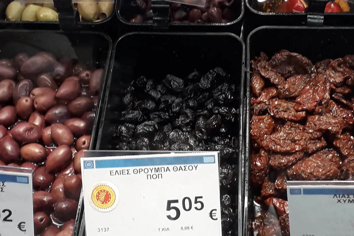 Wrinkled Thasos throuba olives on sale in a Greek supermarket, next to other black olives